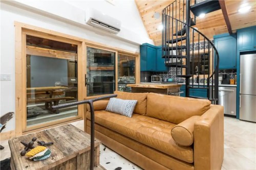 Cozy interior featuring a leather sofa, spiral staircase, and modern kitchen with blue cabinets and wooden accents.