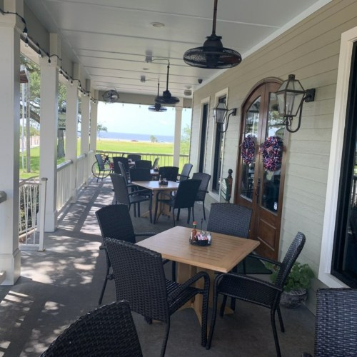 A cozy outdoor dining area with tables and chairs, surrounded by greenery and a view of the water.