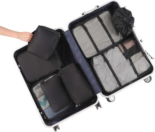 A partially packed suitcase with organized compartments and packing cubes, showing a hand placing an item inside.