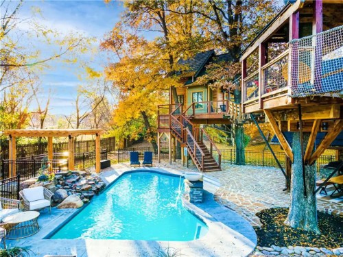 A serene backyard with a pool, surrounded by autumn trees and a wooden treehouse, creating a cozy outdoor retreat.