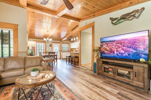 Cozy living room with wooden beams, a TV, and a comfortable sofa, leading to a dining area and kitchen.