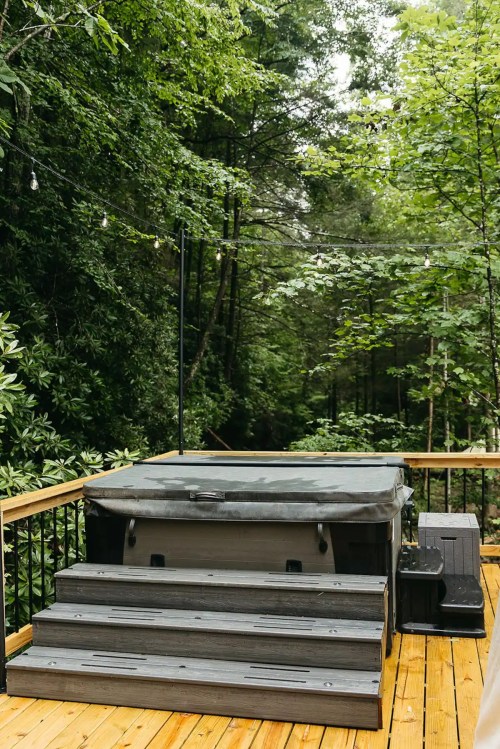 A hot tub on a wooden deck surrounded by lush green trees and soft lighting.