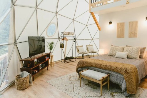 Cozy geodesic dome interior featuring a bed, TV, seating area, and decorative elements in a bright, airy space.