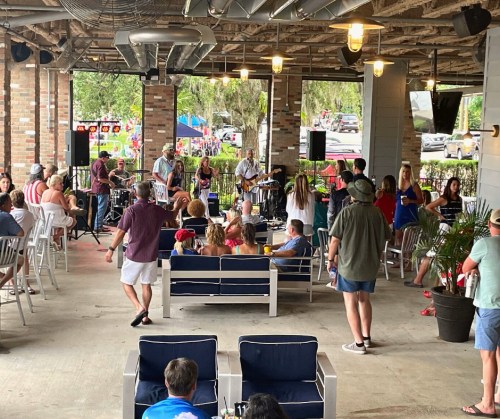 A lively outdoor venue with a band playing, people seated and enjoying the music, and a festive atmosphere.