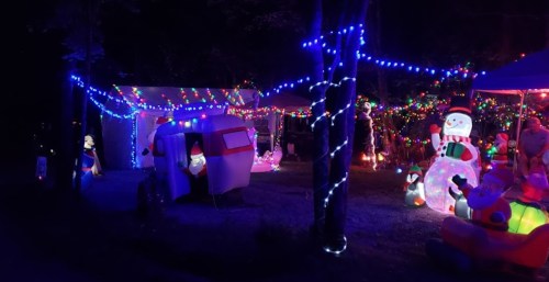 A festive outdoor scene with colorful lights, inflatable decorations, and a decorated camper in a dark setting.