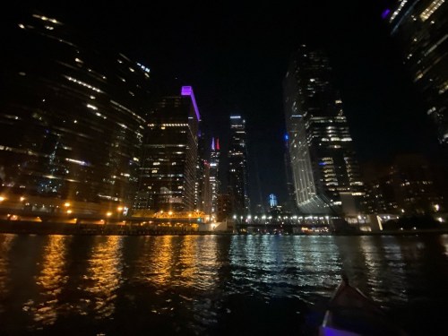 City skyline at night, with illuminated skyscrapers reflecting on the water, creating a vibrant urban scene.