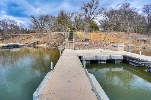 A concrete dock extends into calm water, with trees and a staircase leading to a grassy area in the background.