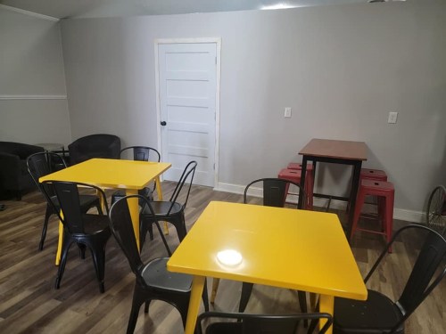 A cozy room with yellow tables, black chairs, and a door, featuring wooden flooring and a simple, modern design.