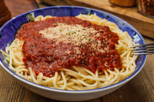 A bowl of spaghetti topped with marinara sauce and grated cheese, served on a wooden table.