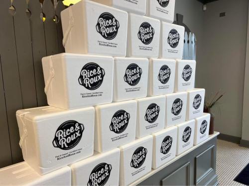 A stack of white foam containers with the logo of "Rice & Roux" displayed prominently on each box.