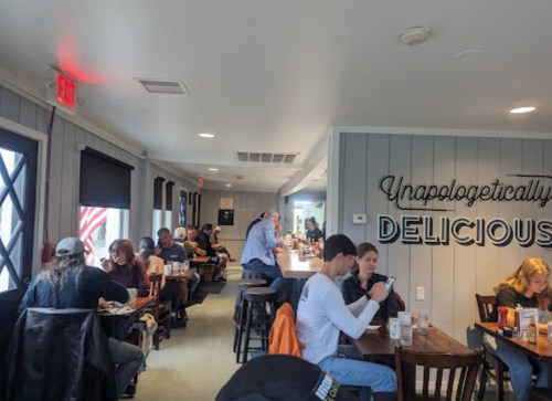 A bustling restaurant interior with diners at tables, featuring a wall sign that reads "Unapologetically Delicious."