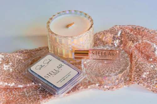 A candle, a perfume bottle, and a compact on a sparkling fabric background.