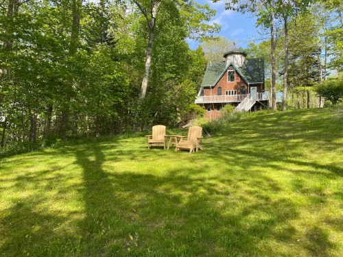 A grassy area with two wooden chairs in front of a large, rustic house surrounded by trees.