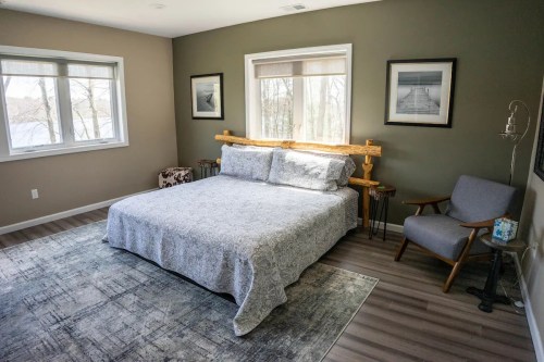 A cozy bedroom featuring a bed with a gray patterned blanket, a wooden headboard, and a gray armchair by the window.