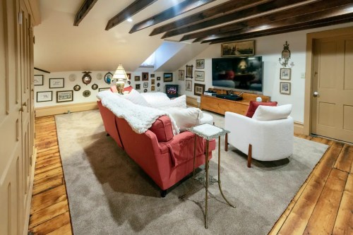 Cozy attic living room with a pink sofa, white armchair, wooden beams, and framed pictures on the walls.