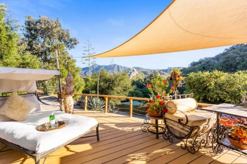 A serene outdoor patio with a lounge chair, potted plants, and a view of mountains under a sunshade.