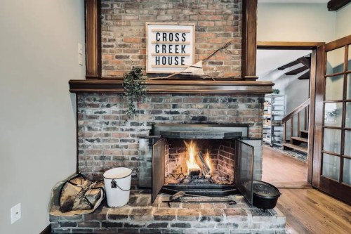 Cozy brick fireplace with a wooden mantel, featuring a sign that reads "Cross Creek House" and a warm fire burning inside.