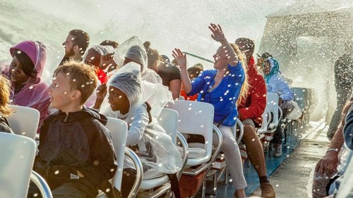 A group of people on a boat, some laughing and shielding themselves from splashes of water, enjoying a lively ride.