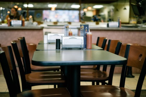 A view of empty tables and chairs in a casual restaurant, with condiments on the tables and a warm atmosphere.