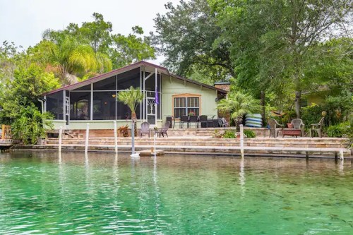 A serene lakeside home with a screened porch, surrounded by lush greenery and a calm, clear water view.