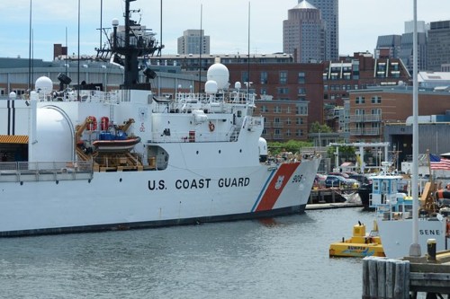 A U.S. Coast Guard ship docked in a harbor with city buildings in the background.
