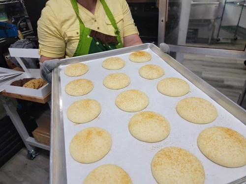 A person in an apron holds a tray of freshly baked cookies, ready to be served.