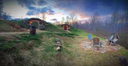 A scenic view of hobbit-style homes on a hillside, with a stone patio and chairs, surrounded by trees and a colorful sky.