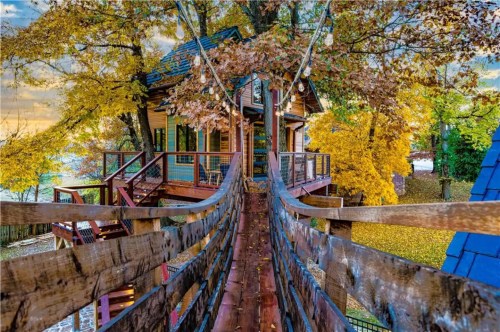 A charming treehouse surrounded by vibrant autumn foliage, connected by a wooden bridge.