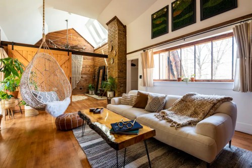 Cozy living room with a hanging chair, wooden accents, plants, and a stylish coffee table. Bright and inviting atmosphere.