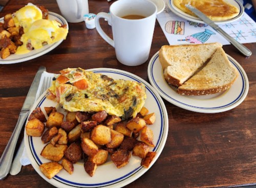 A plate with an omelet, seasoned potatoes, toast, and a cup of coffee on a wooden table.