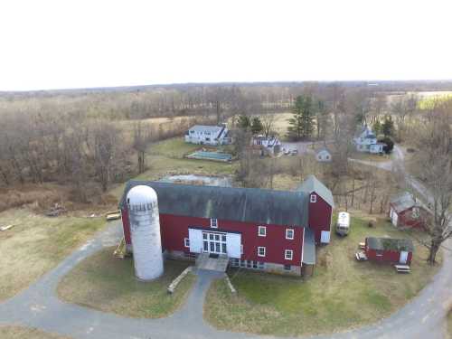 Aerial view of a red barn with a silo, surrounded by fields and several houses in a rural landscape.