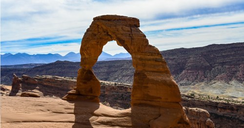 A natural stone arch stands against a backdrop of mountains and blue skies, showcasing the beauty of the desert landscape.