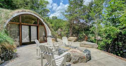 A serene outdoor space with stone seating, a fire pit, and a curved glass structure surrounded by greenery.