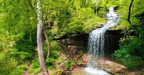 A serene waterfall cascading down rocky cliffs, surrounded by lush green trees and foliage.
