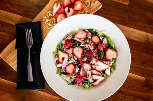 A fresh salad with sliced strawberries, greens, and nuts, served in a white bowl on a wooden table.