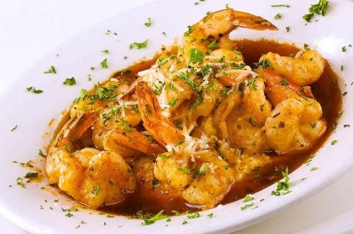 A plate of shrimp in a savory sauce, garnished with herbs and cheese, served over a bed of rice.