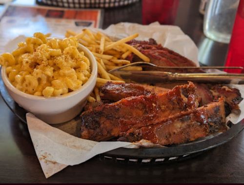 A plate of barbecue ribs with sauce, fries, and a side of creamy macaroni and cheese.