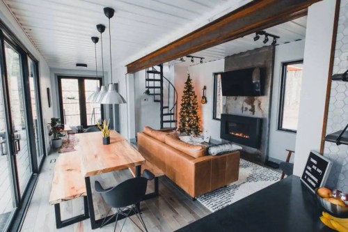 Modern living space featuring a wooden dining table, leather sofa, spiral staircase, and a Christmas tree by a fireplace.