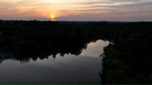 A serene sunset over a calm river, reflecting the colorful sky and surrounded by lush greenery.