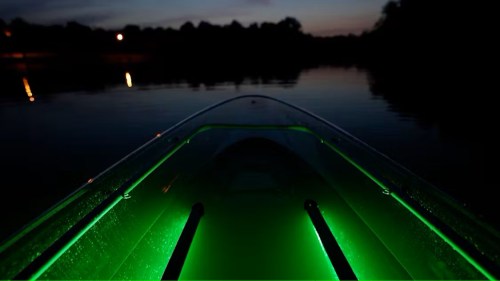 A glowing green kayak on calm water at dusk, with reflections of lights in the background.