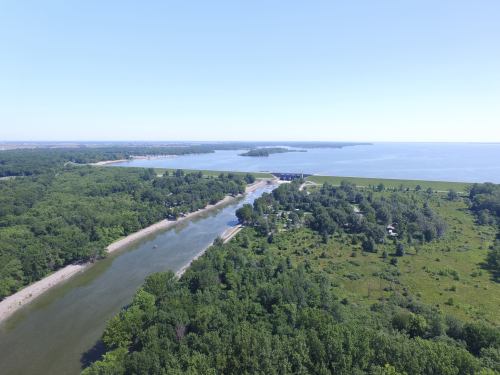 Aerial view of a river winding through lush greenery, leading to a large body of water under a clear blue sky.