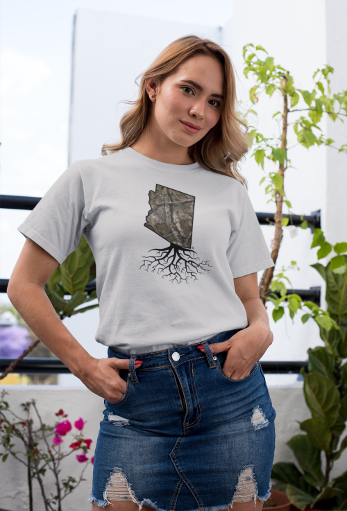 A person wearing a gray t-shirt with a graphic of Arizona and roots, standing in a garden with plants.