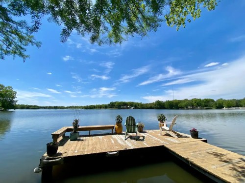 A serene lakeside view from a wooden dock with chairs and potted plants under a clear blue sky.