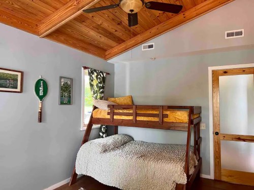 Cozy bedroom featuring a wooden bunk bed, a double bed below, and wooden ceiling beams. Decor includes framed art.