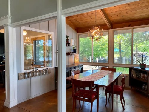 Bright dining area with a wooden table, chairs, and large windows overlooking a scenic outdoor view.