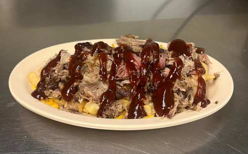 A plate of loaded fries topped with pulled pork and drizzled with barbecue sauce.