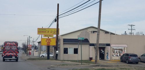 A restaurant with a drive-thru sign, featuring a mural on the side and parked cars on the street.