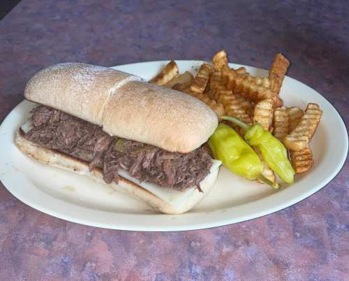 A sandwich filled with shredded beef on a hoagie roll, served with crinkle-cut fries and a pepper on the side.