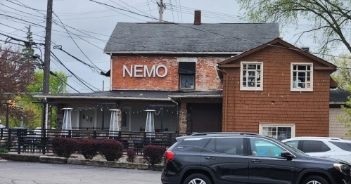 A brick building with a sign reading "NEMO," featuring a wooden addition and parked cars in front.