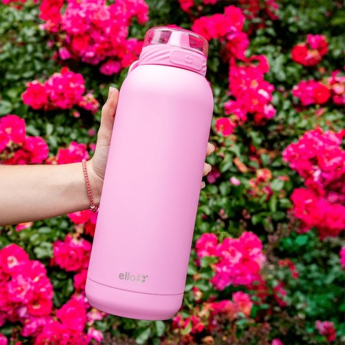 A hand holds a pink water bottle against a backdrop of vibrant pink flowers.